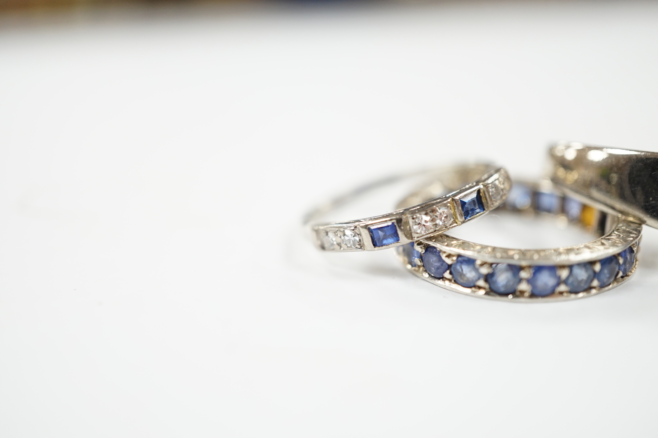 An 18k white metal, emerald and diamond set dress ring, size O, a white metal and sapphire set full eternity ring (stones missing) and an 18ct, sapphire and diamond set half hoop ring, gross weight 10 grams.
